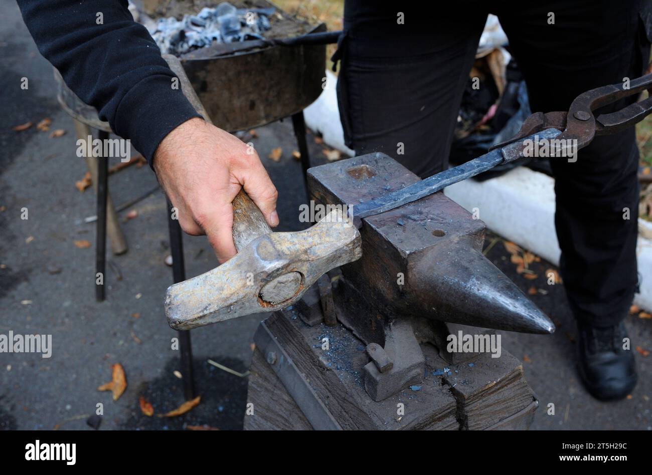 Le mani di un fabbro che tengono le pinze e un martello che forgia una lama di billetta metallica di un coltello su un'incudine Foto Stock