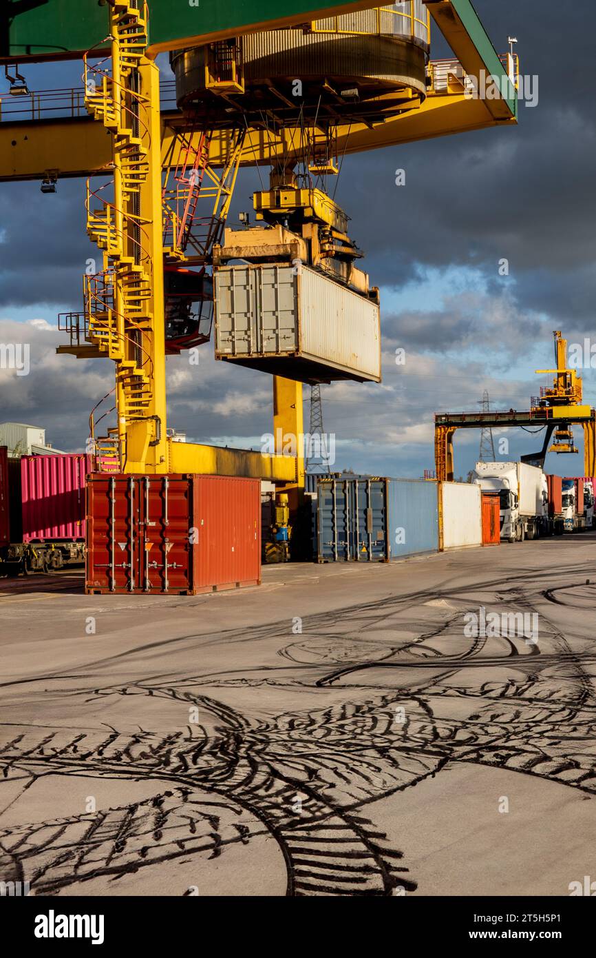 Una gru industriale che solleva le scatole di container per la spedizione e le carica sui carrelli per il trasporto su strada nel Regno Unito e nel mondo Foto Stock