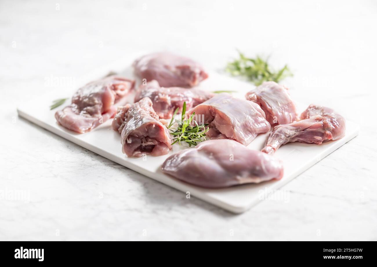 Pezzi di coniglio porzionato con rosmarino su un tagliere bianco. Foto Stock