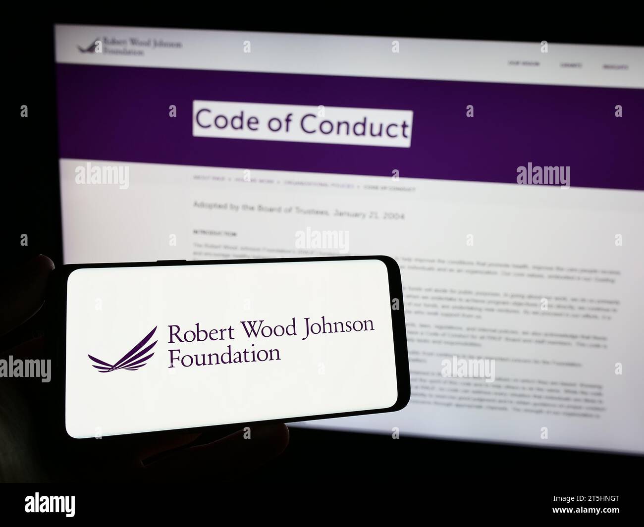 Persona che possiede uno smartphone con il logo dell'organizzazione statunitense Robert Wood Johnson Foundation (RWJF) davanti al sito Web. Concentrarsi sul display del telefono. Foto Stock