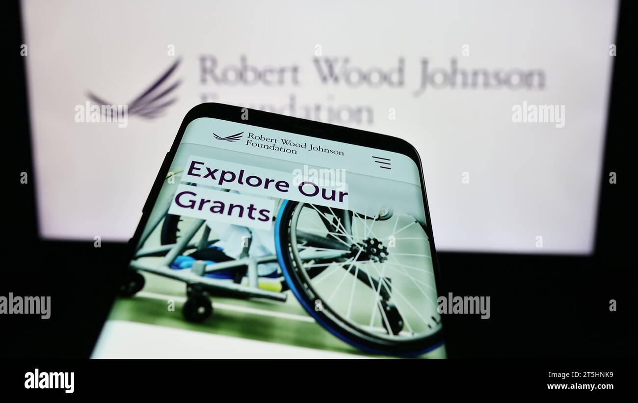 Telefono cellulare con sito web dell'organizzazione statunitense Robert Wood Johnson Foundation (RWJF) davanti al logo. Mettere a fuoco in alto a sinistra sul display del telefono. Foto Stock