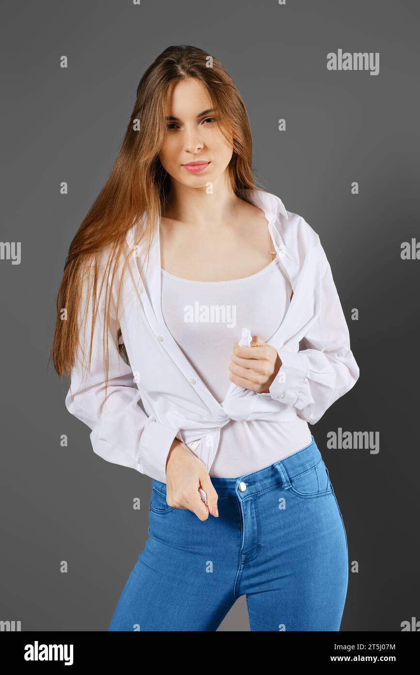 Giovane donna giocosa che si lega a una camicia in piedi in studio su sfondo grigio Foto Stock