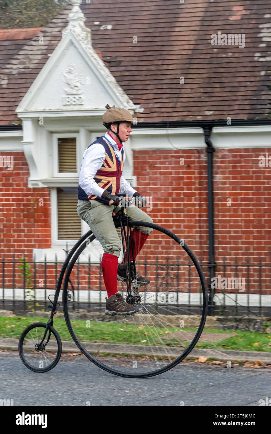 5 novembre 2023. I partecipanti alla corsa di auto da Londra a Brighton Veteran Car Run 2023 guidando attraverso West Sussex, Inghilterra, Regno Unito. Il percorso del famoso evento annuale si estende per 60 chilometri circa. Un uomo che cavalca una bicicletta da un penny. Foto Stock