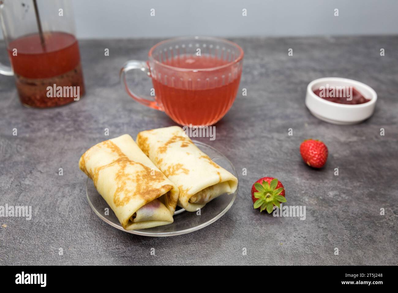 pancake con ripieno di frutti di bosco e fragole, una tazza di tè alla frutta, su un tavolo grigio scuro. Foto Stock