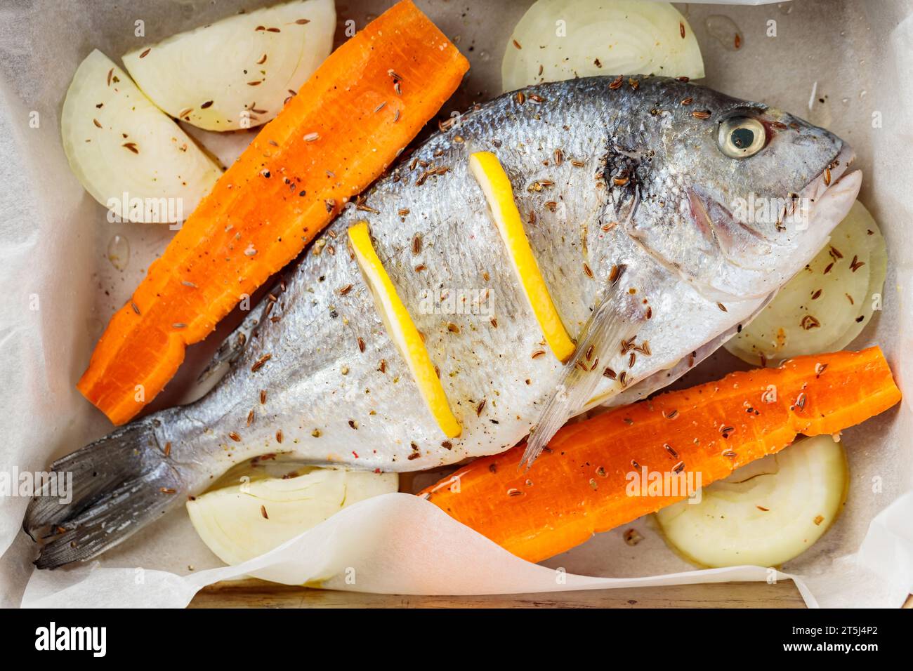 Pesce dorado marinato con verdure e spezie su teglia prima di cuocere. Primo piano Foto Stock