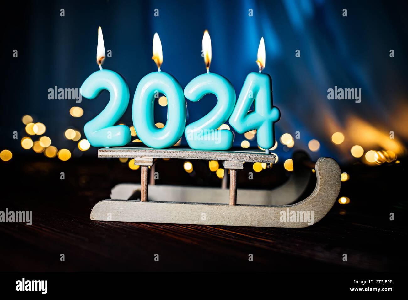 Sfondo natalizio felice anno nuovo 2024 di candele blu accese su una slitta su uno sfondo blu con luci natalizie. Festeggiamo le vacanze di Capodanno, close-u Foto Stock