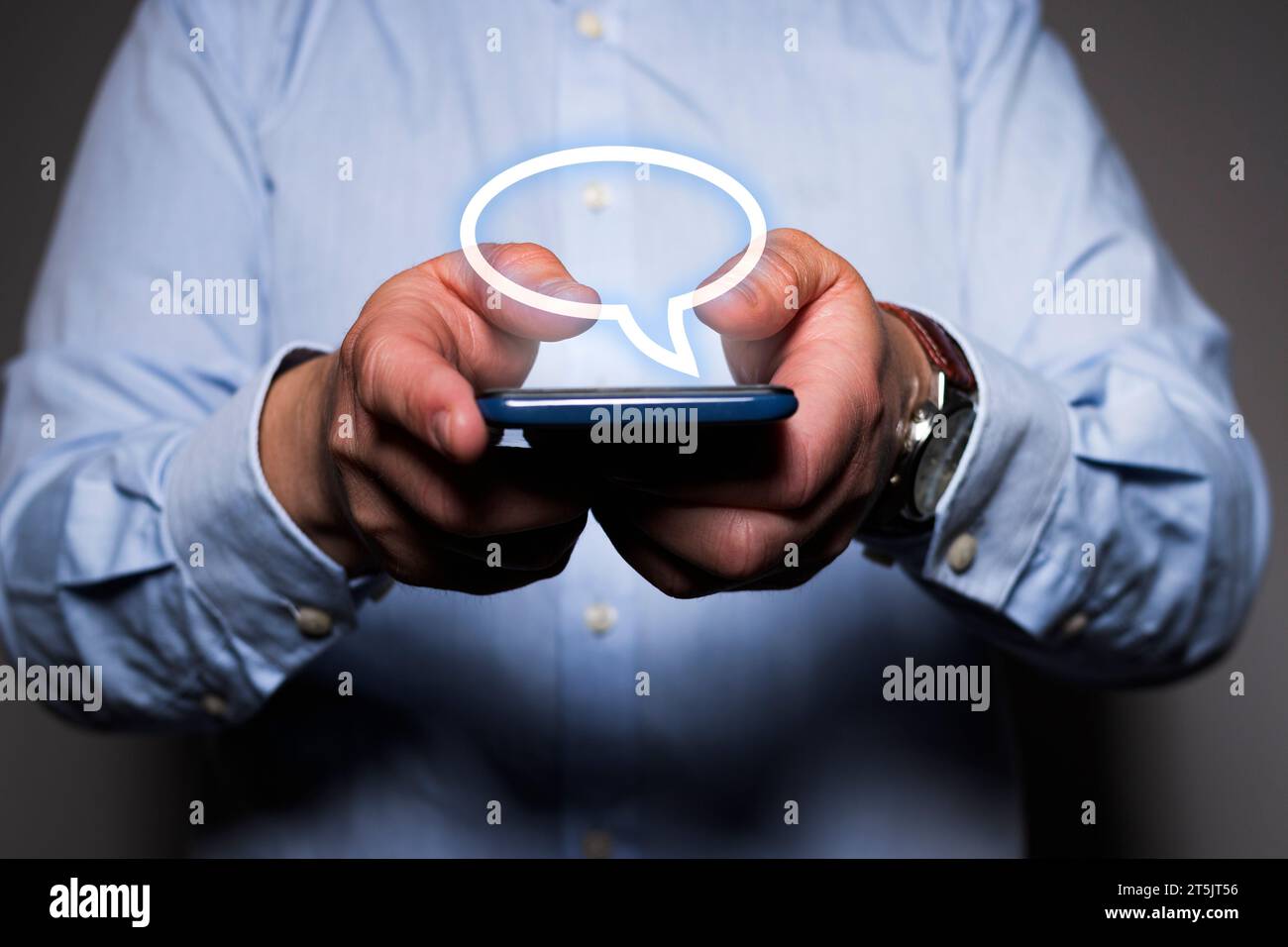 Primo piano delle mani di un uomo caucasico irriconoscibile che tiene in mano un telefono cellulare mentre vede un'icona fumettistica virtuale fluttuare sopra lo smartphone. Foto Stock