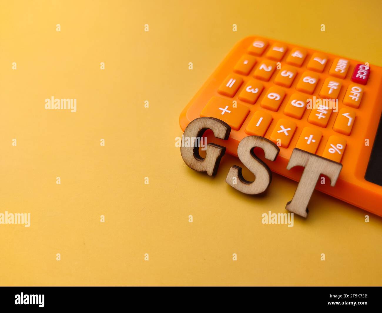 Calcolatrice e parola in legno con testo GST su sfondo giallo. Foto Stock