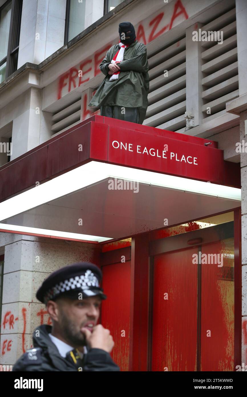 Un attivista protesta contro il baldacchino sopra l'ingresso principale degli uffici, mentre gli agenti di polizia tengono d'occhio la parte sottostante. Gli attivisti di Palestine Action occupano e prendono di mira il gigante italiano dell'industria degli armamenti Leonardo nel loro quartier generale di Londra e li chiudono. Leonardo rifornisce Israele con jet da combattimento e armi attualmente in uso a Gaza. Palestine Action chiede che le compagnie di armamento che forniscono armi a Israele chiudano definitivamente. Hanno annunciato che le società che vendono armi alla forza di difesa israeliana e alle loro società partner saranno prese di mira con azioni dirette. Queste azioni ar Foto Stock