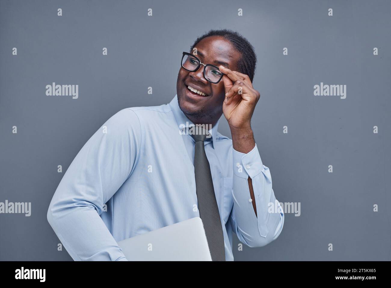 giovane afro-americano su sfondo grigio che sorride aggiustando gli occhiali Foto Stock