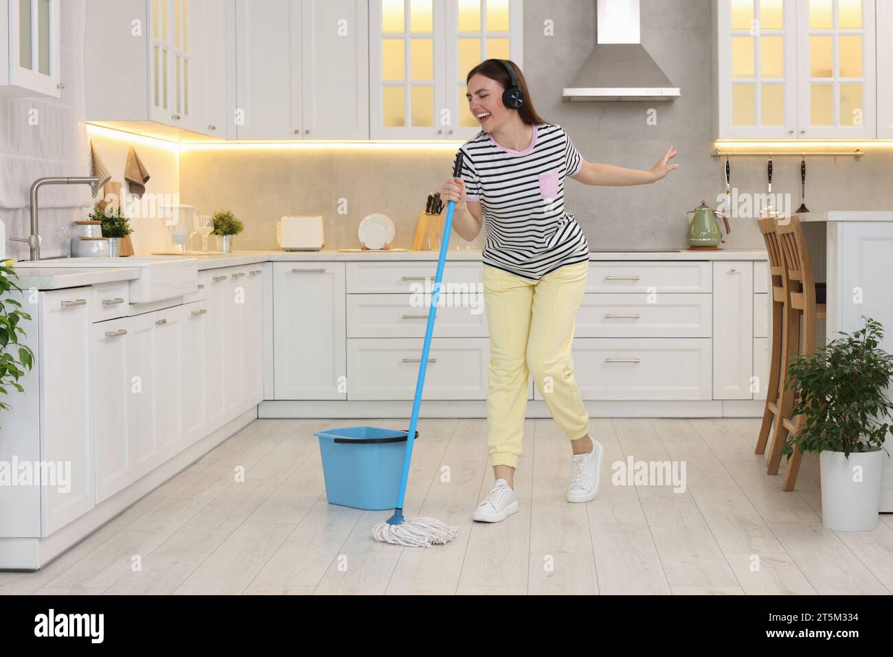 Mi piace pulire. Donna felice con le cuffie che balla con lo spazzolone in cucina Foto Stock