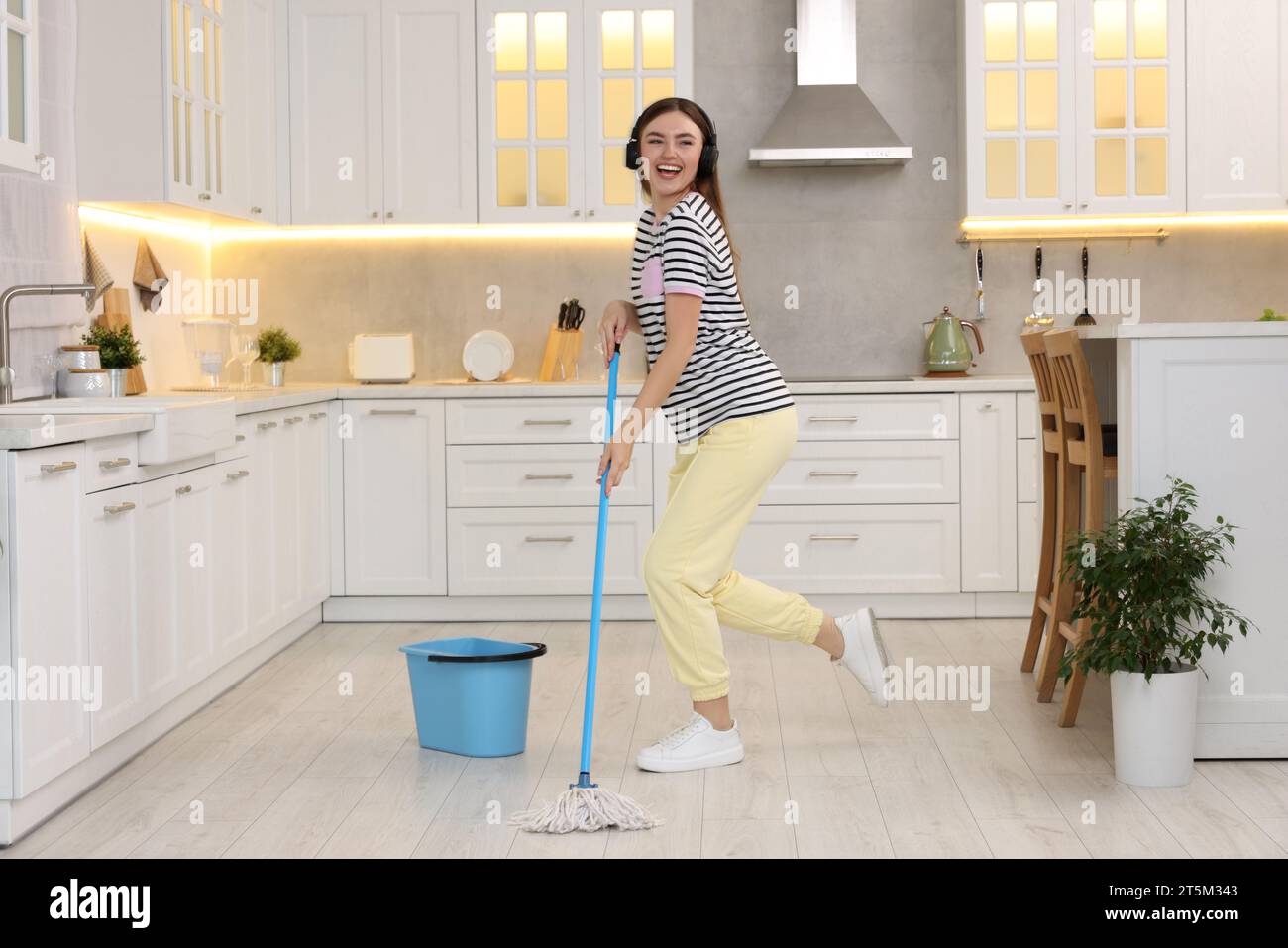 Mi piace pulire. Donna felice con le cuffie che balla con lo spazzolone in cucina Foto Stock