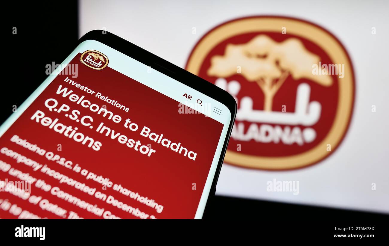 Telefono cellulare con pagina Web dell'azienda casearia e alimentare del Qatar Baladna davanti al logo aziendale. Mettere a fuoco in alto a sinistra sul display del telefono. Foto Stock