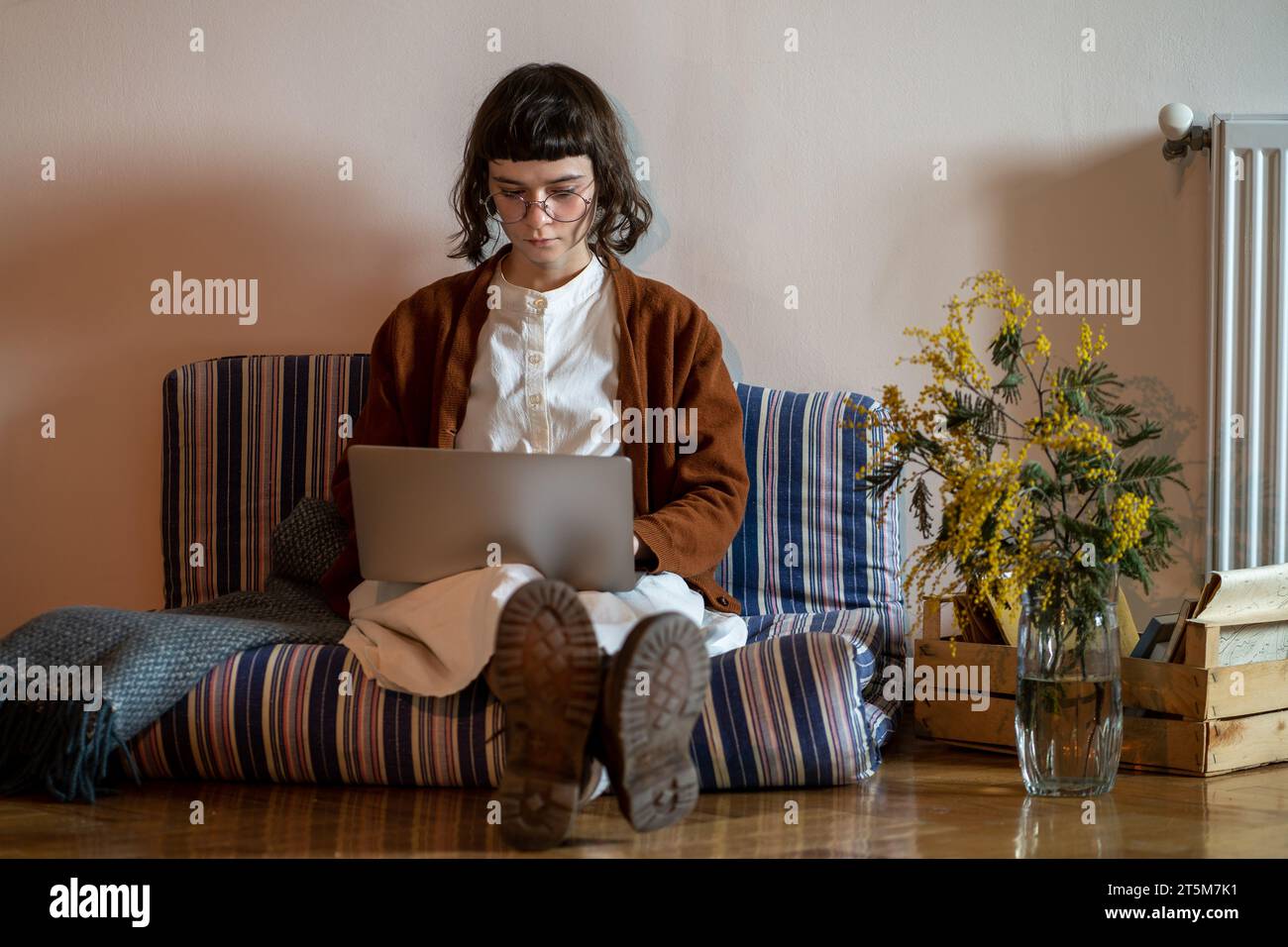 Ragazza hipster adolescente impegnata seduta comodamente sul materasso con un computer portatile, che lavora, studia da casa Foto Stock