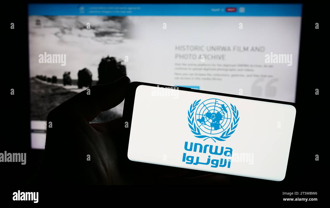 Persona che possiede uno smartphone con il logo dell'agenzia delle Nazioni Unite per i rifugiati plalestini UNRWA davanti al sito Web. Concentrarsi sul display del telefono. Foto Stock
