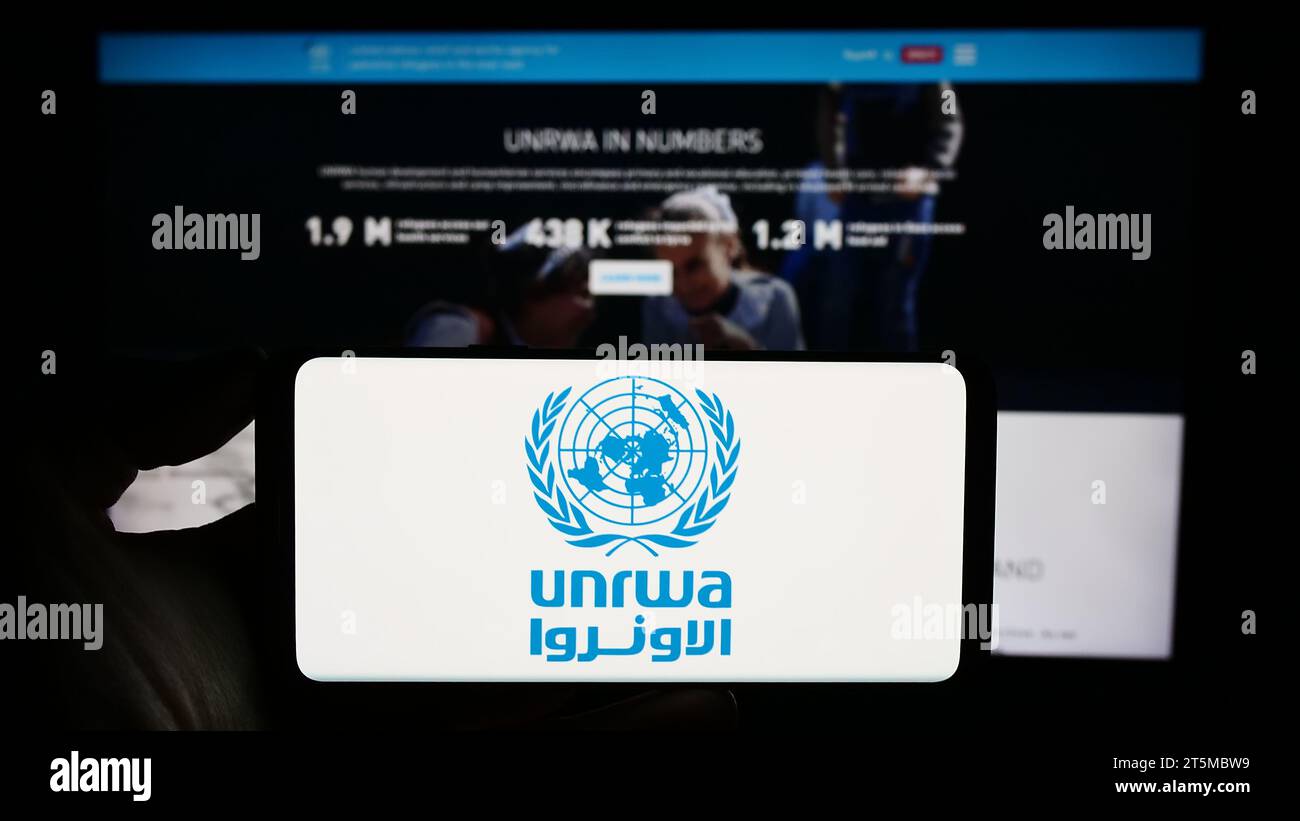 Persona che possiede un telefono cellulare con il logo dell'agenzia delle Nazioni Unite per i rifugiati plalestini UNRWA davanti alla pagina web. Concentrarsi sul display del telefono. Foto Stock