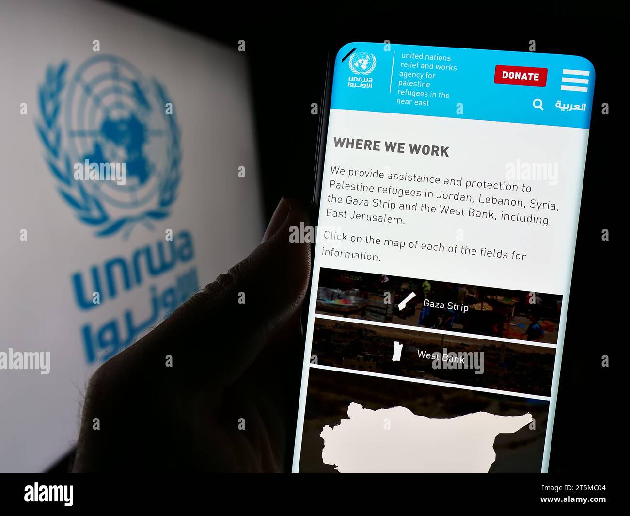 Persona in possesso di un cellulare con la pagina web dell'agenzia delle Nazioni Unite per i rifugiati plalestini UNRWA davanti al logo. Concentrarsi sul centro del display del telefono. Foto Stock