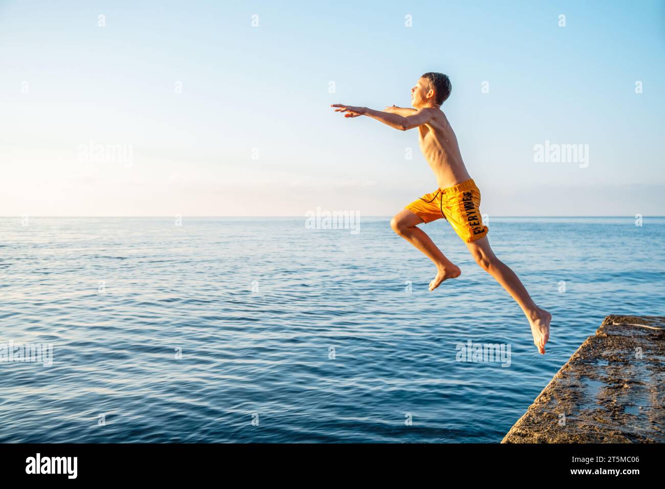 Il momento in cui uno scolaro salta dal molo di pietra in mare facendo trucchi all'alba in sequenza di immagini combinate Foto Stock