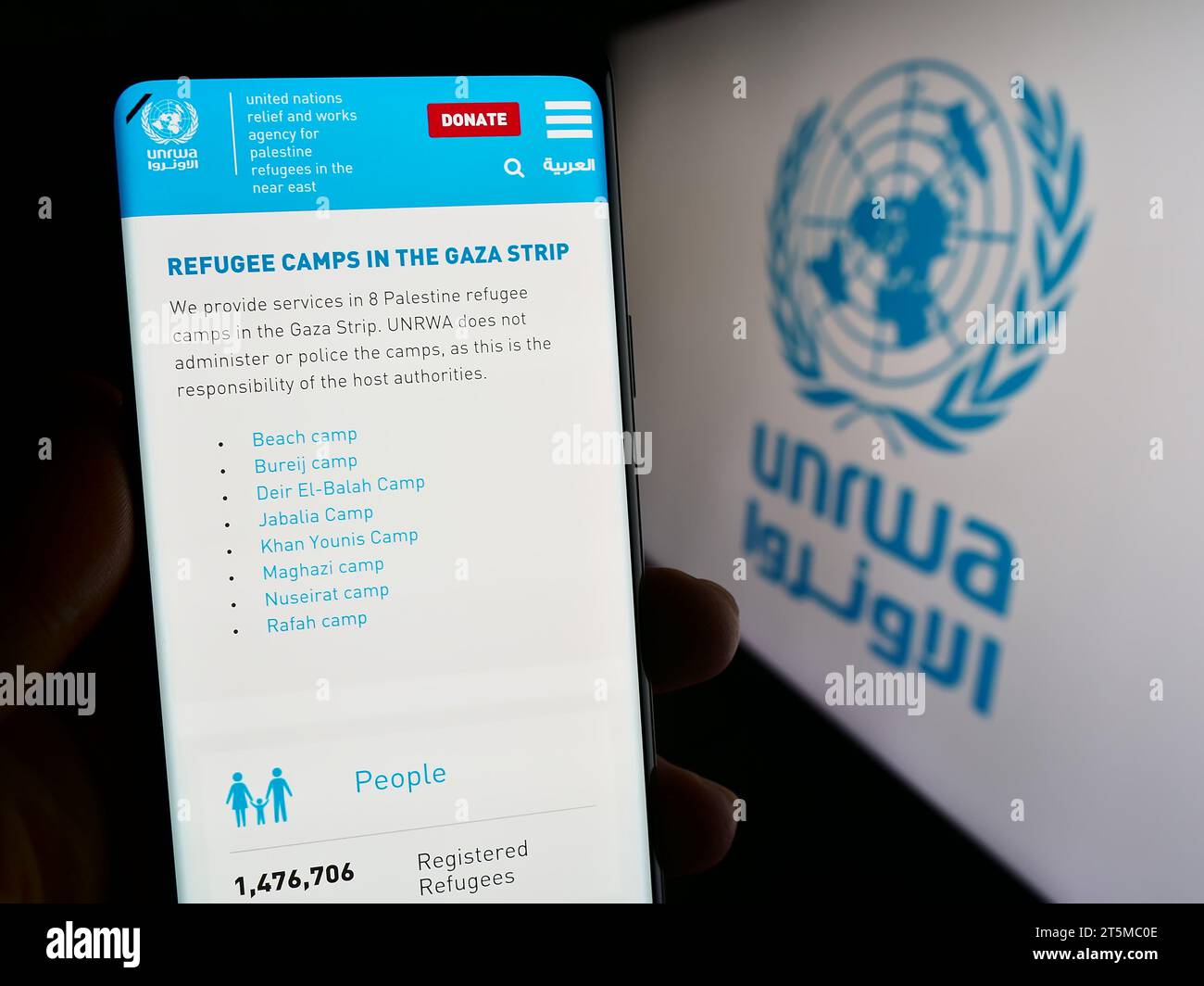 Persona che possiede uno smartphone con una pagina Web dell'agenzia delle Nazioni Unite per i rifugiati plalestini UNRWA davanti al logo. Concentrarsi sul centro del display del telefono. Foto Stock