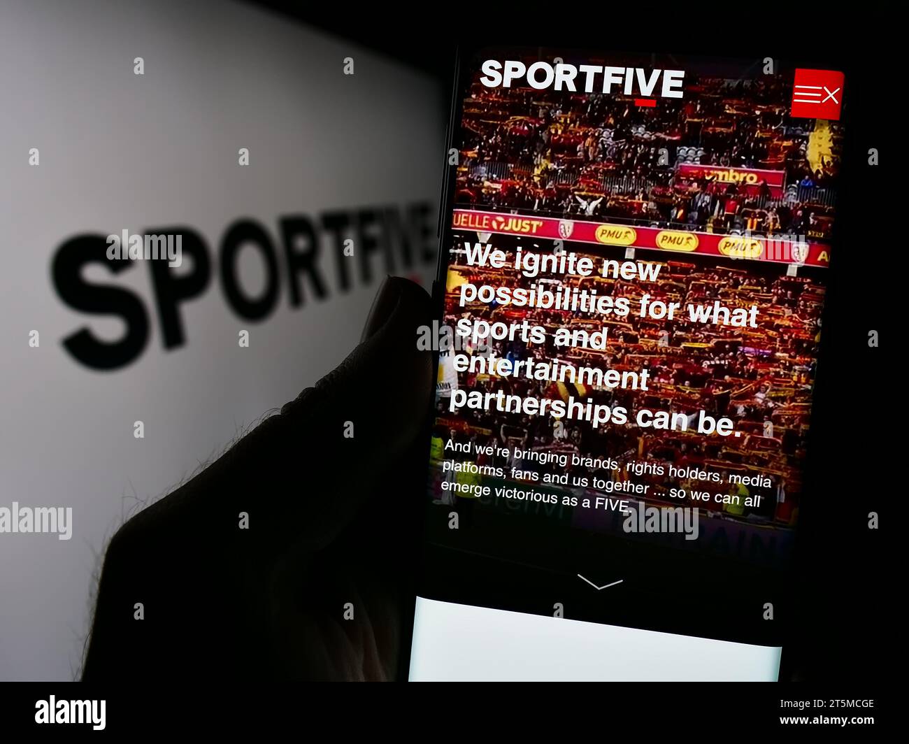 Persona che possiede il cellulare con la pagina Web della società internazionale di marketing sportivo Sportfive davanti al logo. Concentrarsi sul centro del display del telefono. Foto Stock