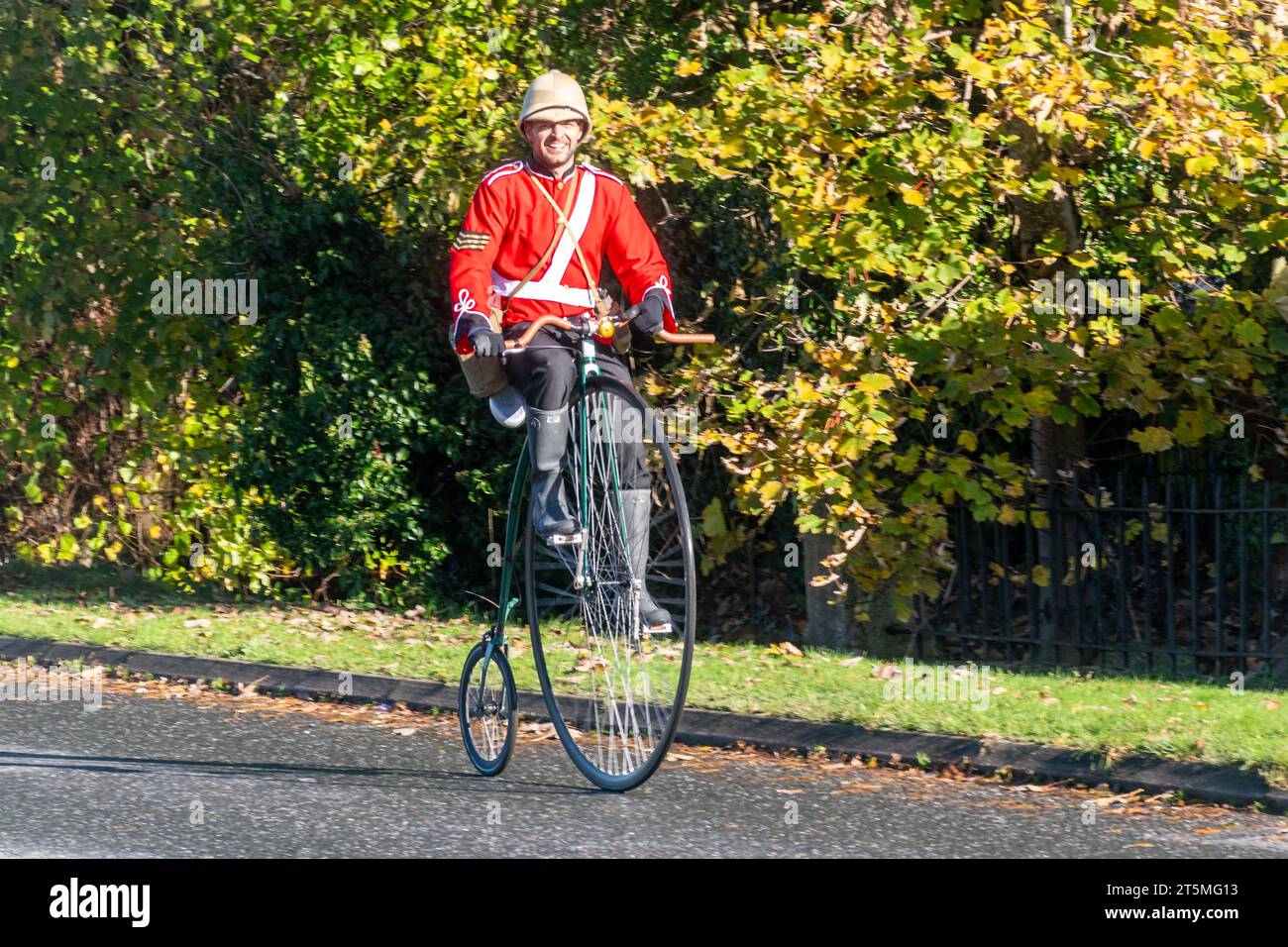 5 novembre 2023. I partecipanti alla corsa di auto da Londra a Brighton Veteran Car Run 2023 guidando attraverso West Sussex, Inghilterra, Regno Unito. Il percorso del famoso evento annuale si estende per 60 chilometri circa. Un uomo che cavalca una bicicletta da un penny che indossa una tunica e un casco dell'esercito britannico vittoriano Foto Stock