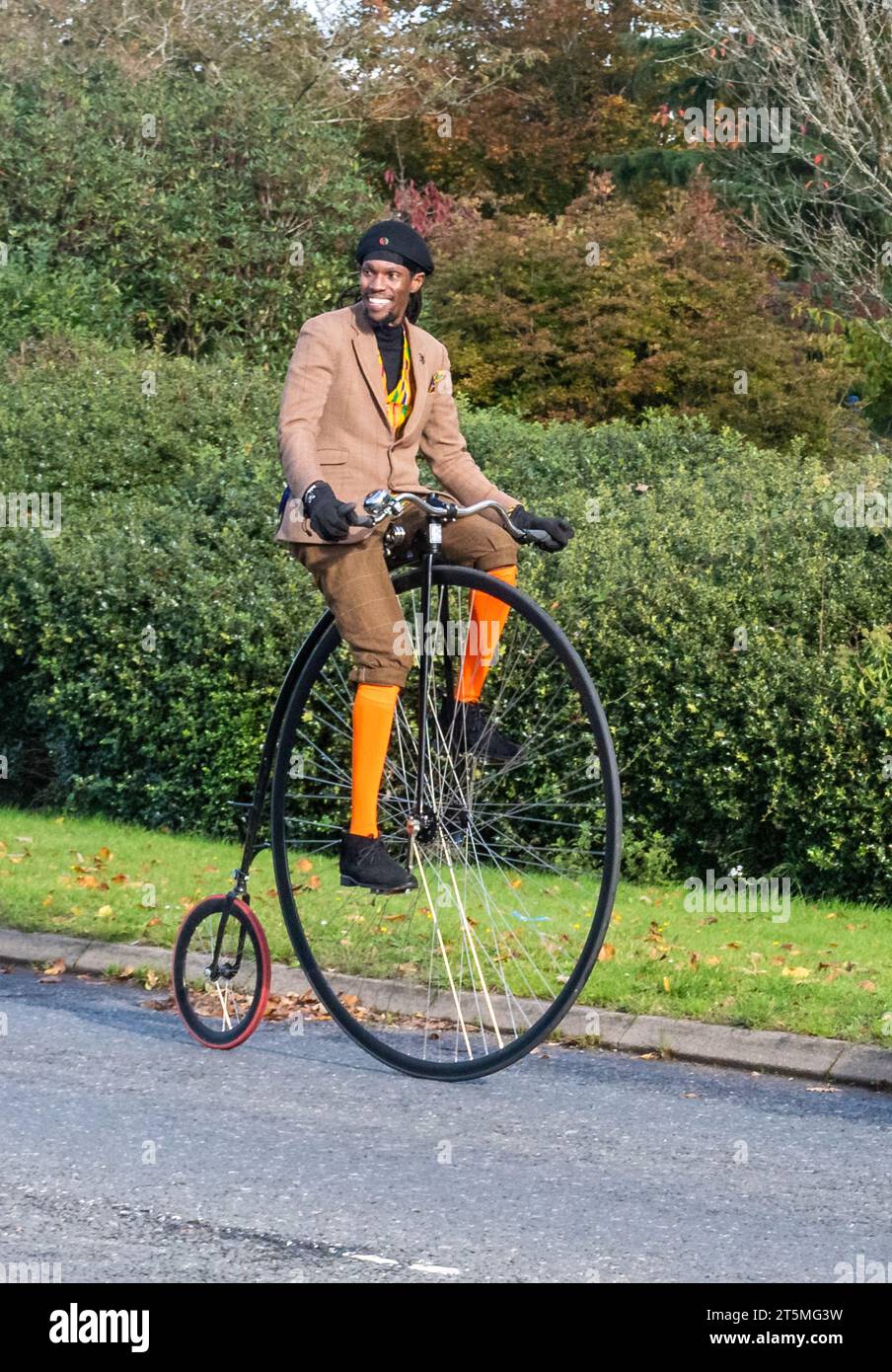 5 novembre 2023. I partecipanti alla corsa di auto da Londra a Brighton Veteran Car Run 2023 guidando attraverso West Sussex, Inghilterra, Regno Unito. Il percorso del famoso evento annuale si estende per 60 chilometri circa. Un uomo che cavalca una bicicletta da un penny. Foto Stock