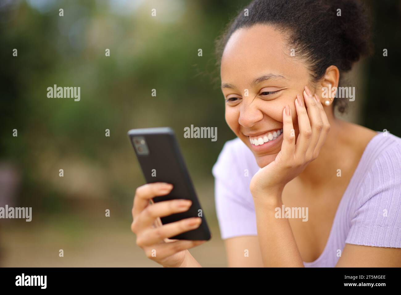 Felice donna nera che legge un messaggio al telefono in un parco Foto Stock
