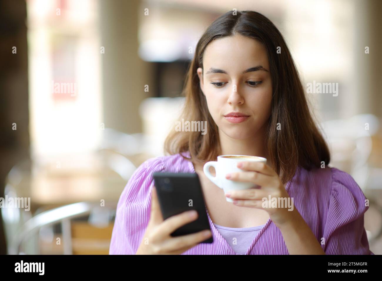 Ritratto frontale di una donna seria che controlla il telefono mentre beve in una terrazza del bar Foto Stock