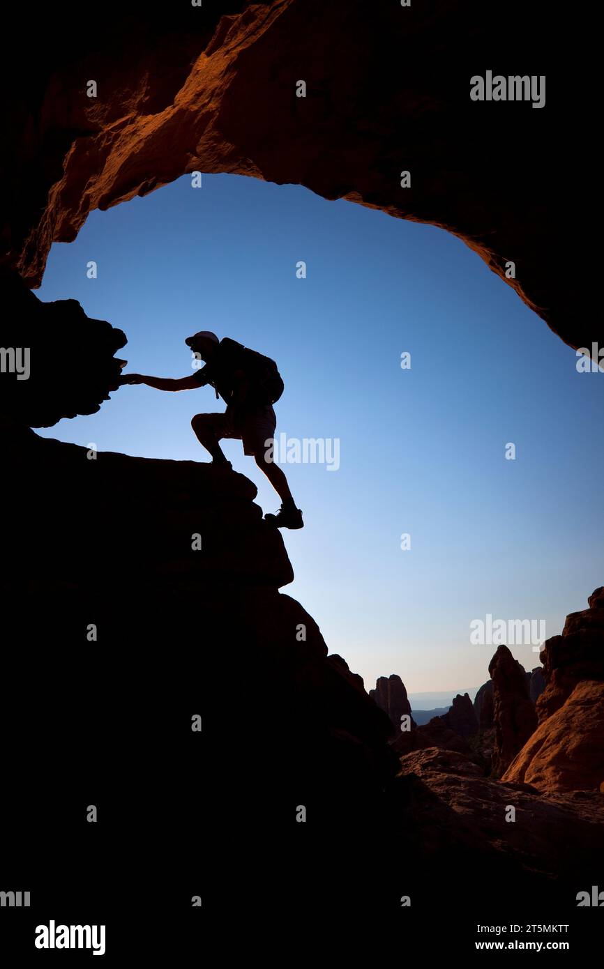 Un escursionista sagomato si arrampica sotto un arco di roccia naturale nell'Arches National Park, Utah. Foto Stock