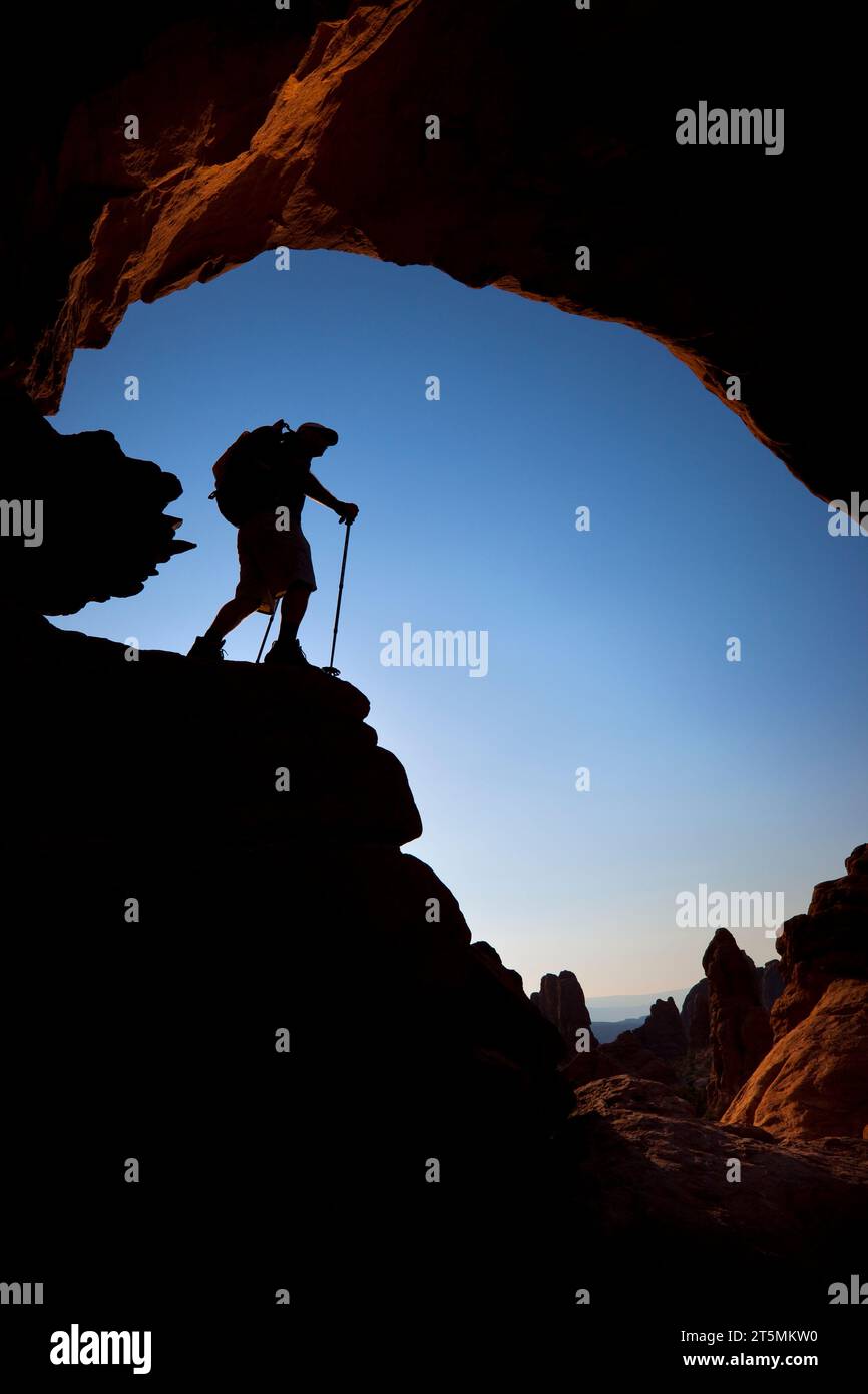 Escursionista sagomato che si trova sotto un arco di roccia naturale nell'Arches National Park, Utah. Foto Stock