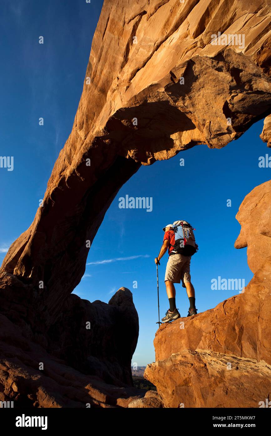 Escursionista che si trova sotto un arco di roccia naturale nel Parco Nazionale di Arches, Utah. Foto Stock