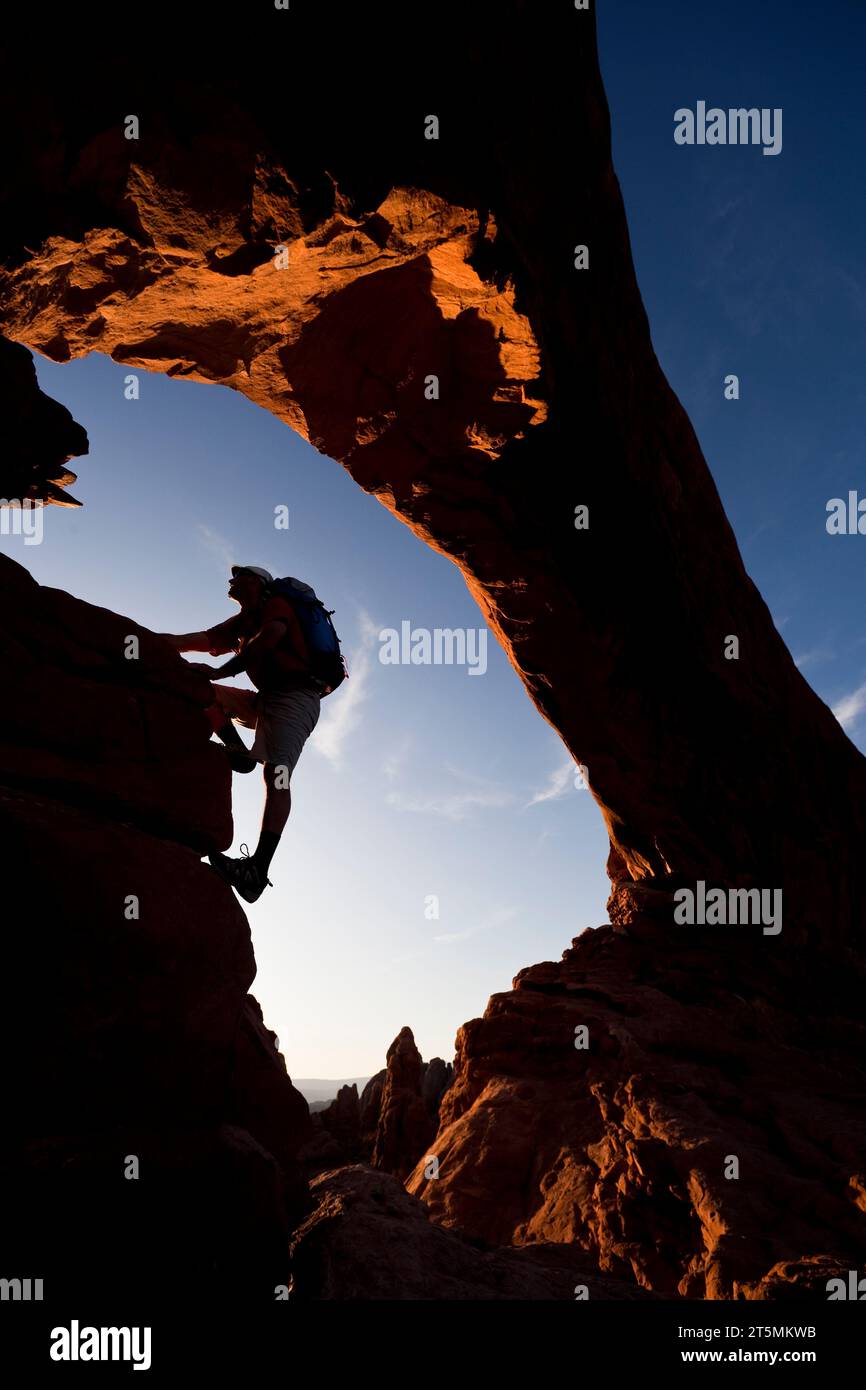 Un escursionista sagomato si arrampica sotto un arco di roccia naturale nell'Arches National Park, Utah. Foto Stock