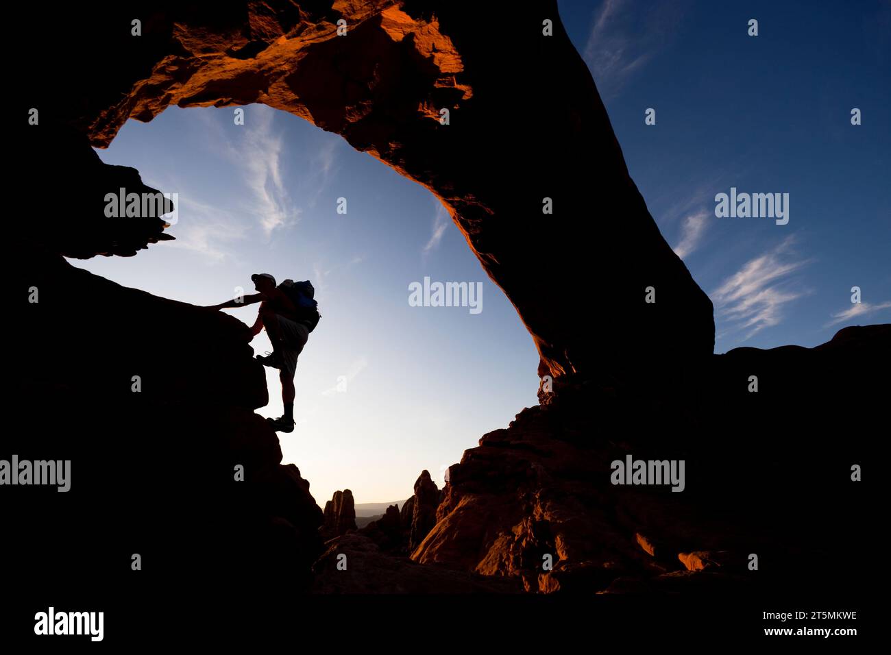 Un escursionista sagomato si arrampica sotto un arco di roccia naturale nell'Arches National Park, Utah. Foto Stock