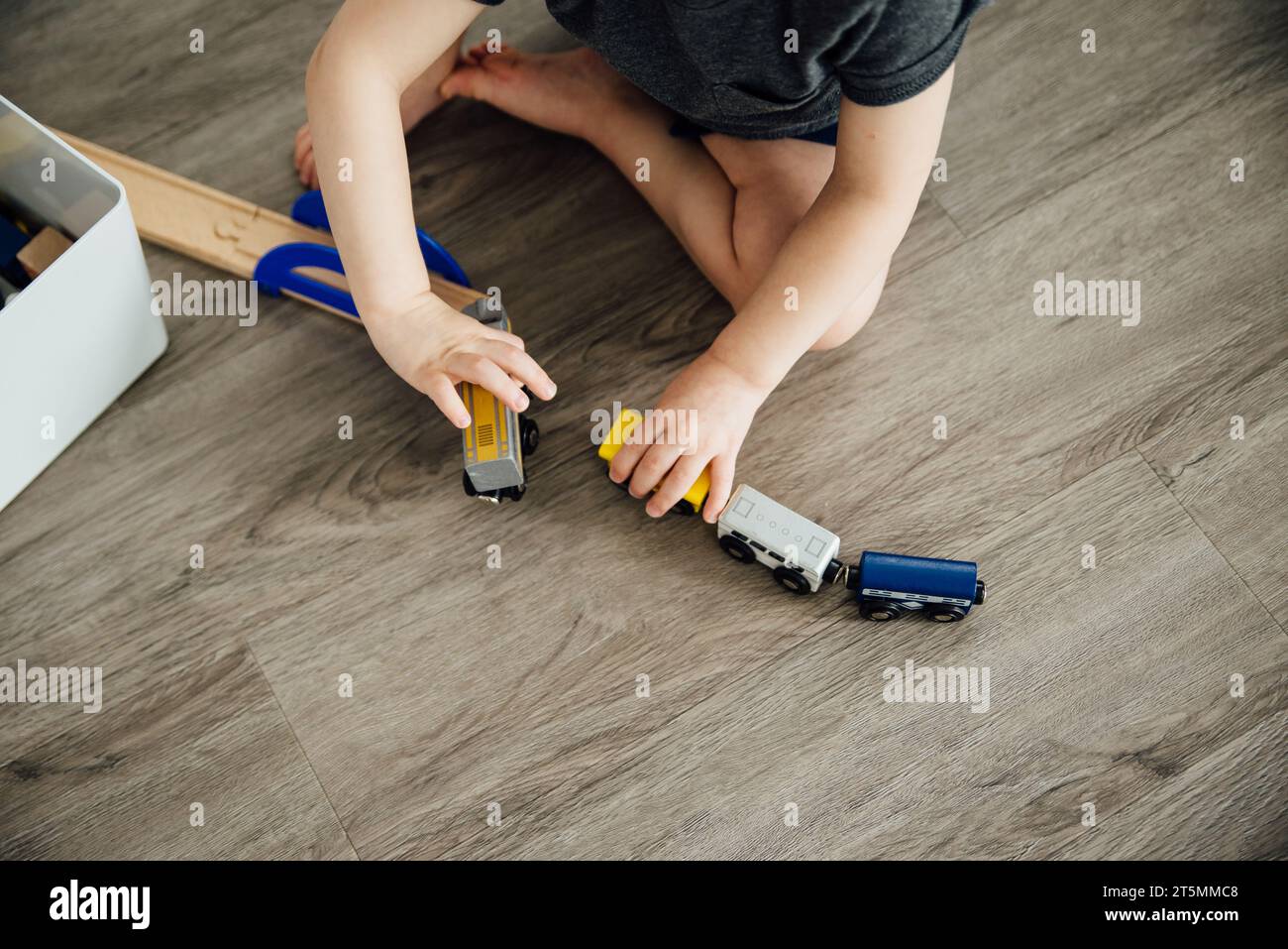 Vista dall'alto di un bambino piccolo che gioca con i treni in legno allineati Foto Stock