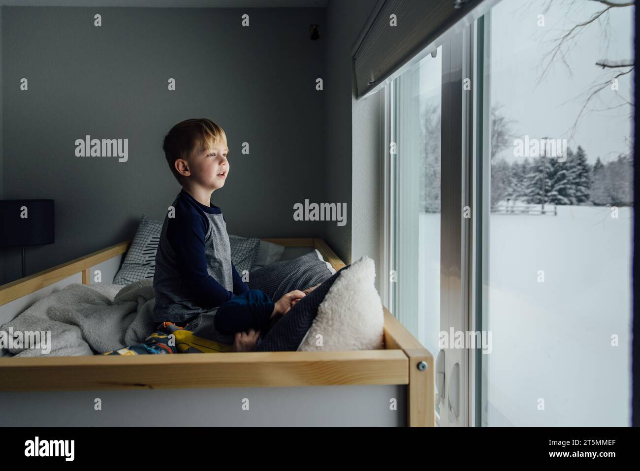 La vista laterale del bambino seduto sul letto si affacciava sulla finestra Foto Stock