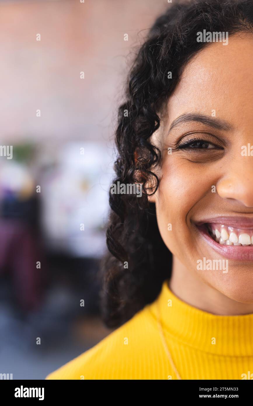 Mezza faccia di felice stilista birazziale in piedi e sorridente in uno studio soleggiato Foto Stock