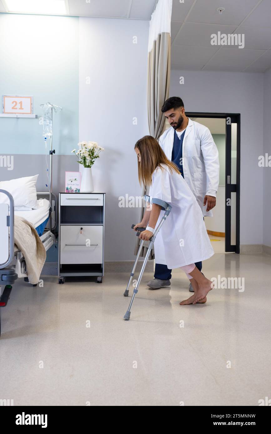 Medico maschile diversificato osservando la ragazza uso del paziente stampelle in reparto ospedaliero, copia spazio Foto Stock