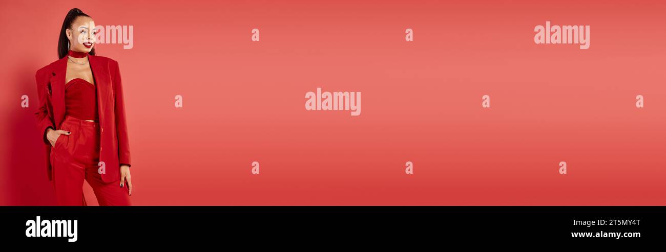 felice donna afro-americana in posa con la mano in tasca di pantaloni vestito su sfondo rosso, banner Foto Stock
