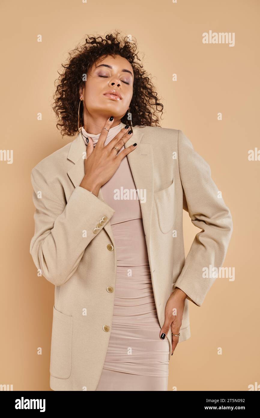 moda autunnale, donna afro-americana bruna con gli occhi chiusi in posa dolcevita e blazer Foto Stock