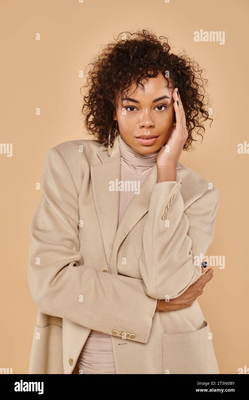 moda autunnale, elegante donna afro-americana in posa con dolcevita e blazer sullo sfondo beige Foto Stock