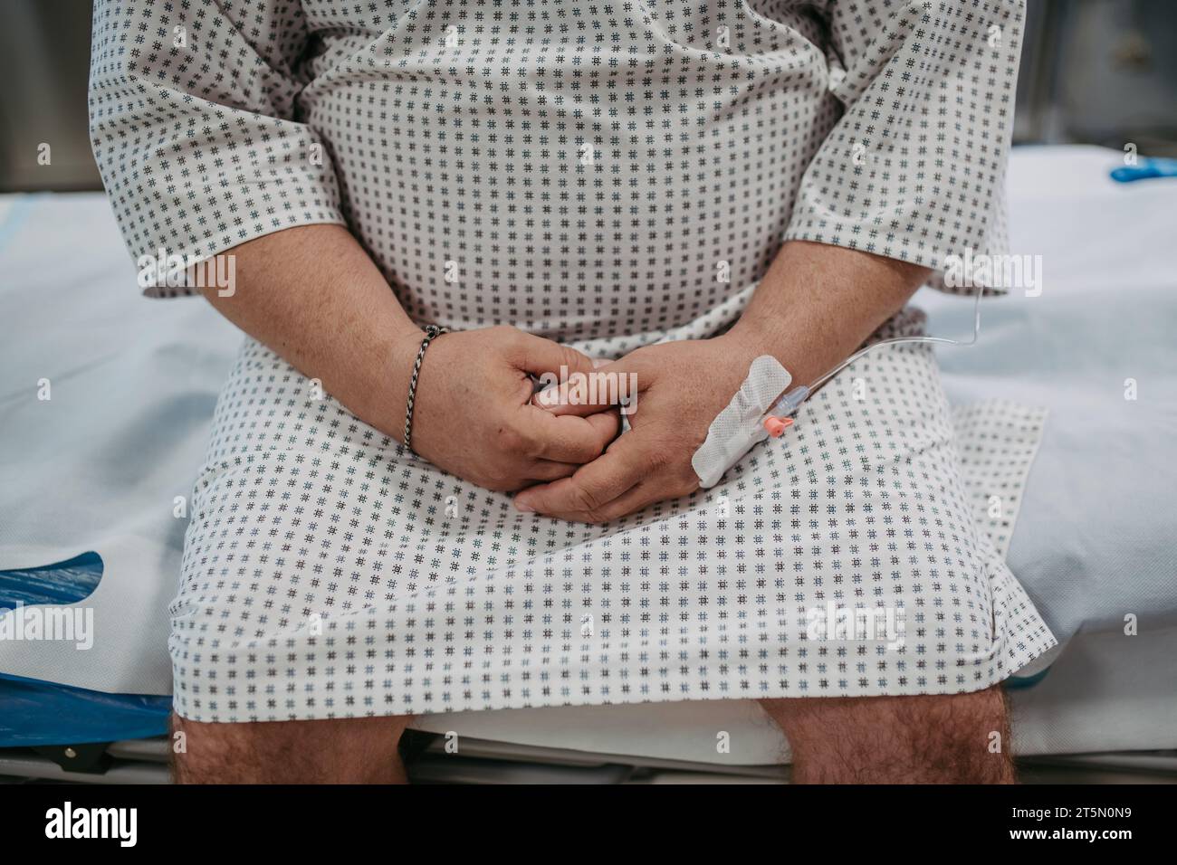 Primo piano di mani di paziente sovrappeso in abito ospedaliero in attesa di visita medica, risultati dei test in ospedale, sensazione di ansia e paura. Foto Stock