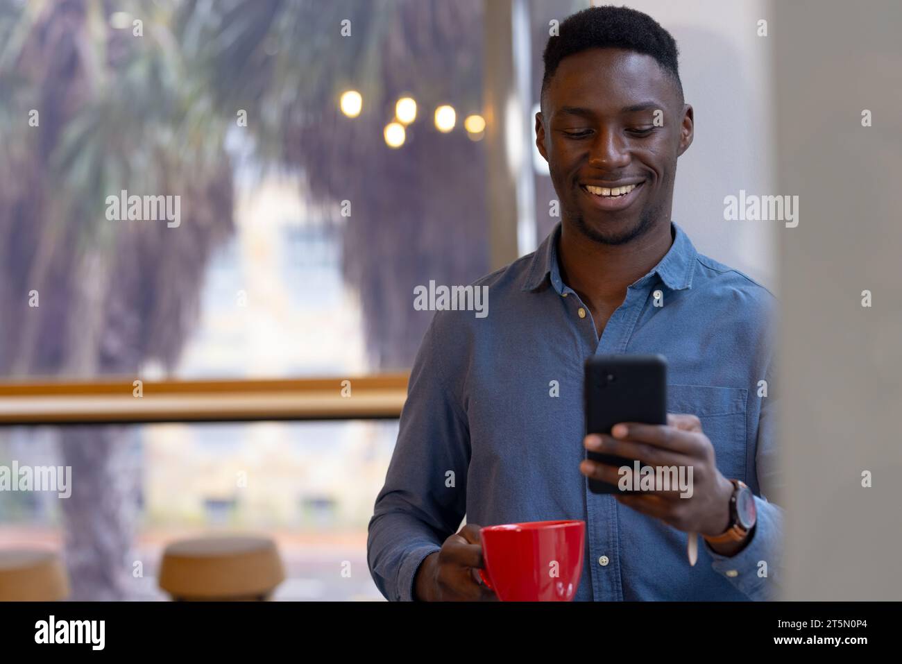 Felice uomo d'affari afroamericano informale con tazza e utilizzo su smartphone in ufficio, spazio copia Foto Stock