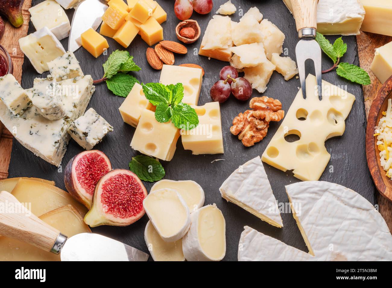 Varietà di formaggi a fette con frutta, menta, noci e taglierini. Un meraviglioso sfondo di formaggi per i vostri progetti. Foto Stock