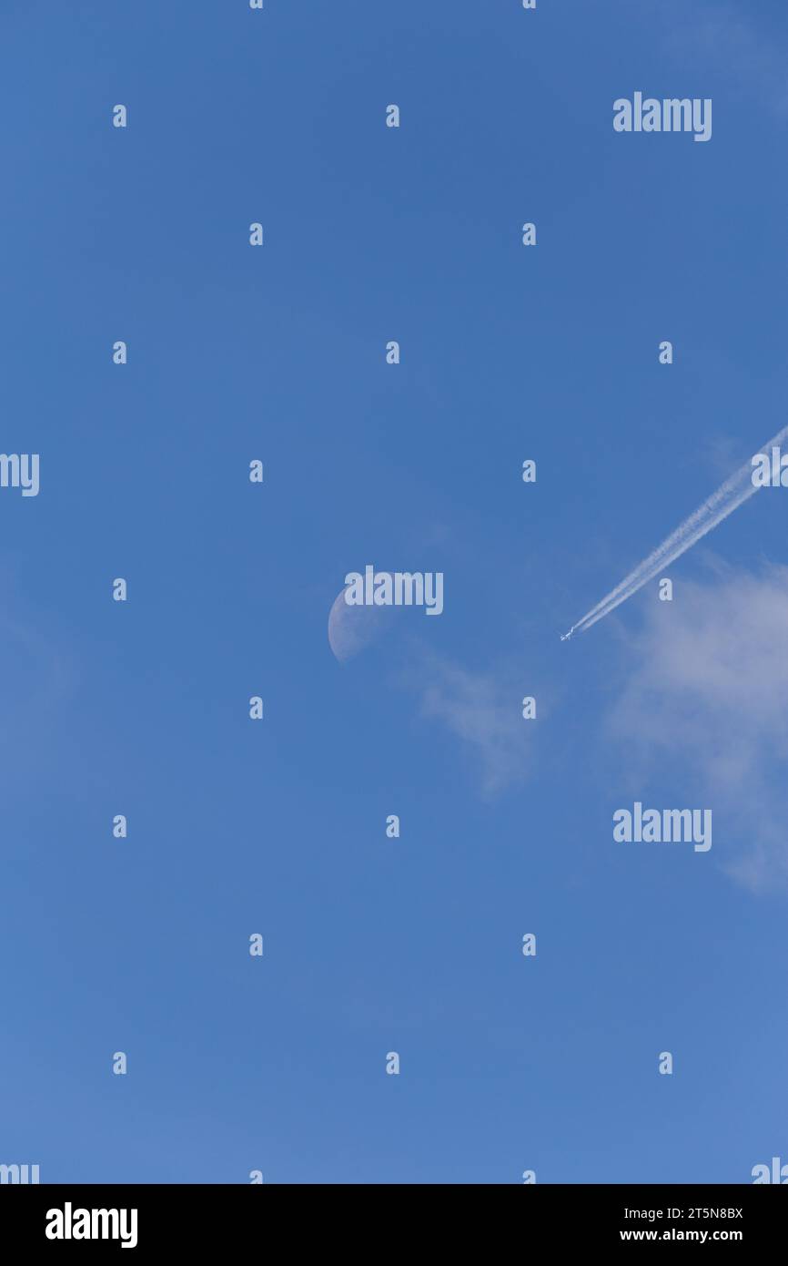 Una perfetta giornata estiva di sole con un aereo e sentieri di condensazione diretti verso una luna visibile in lontananza Foto Stock