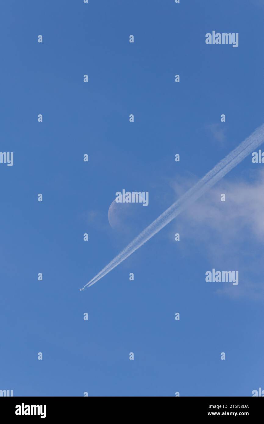 Una perfetta giornata estiva di sole con un aereo e sentieri di condensazione diretti verso una luna visibile in lontananza Foto Stock