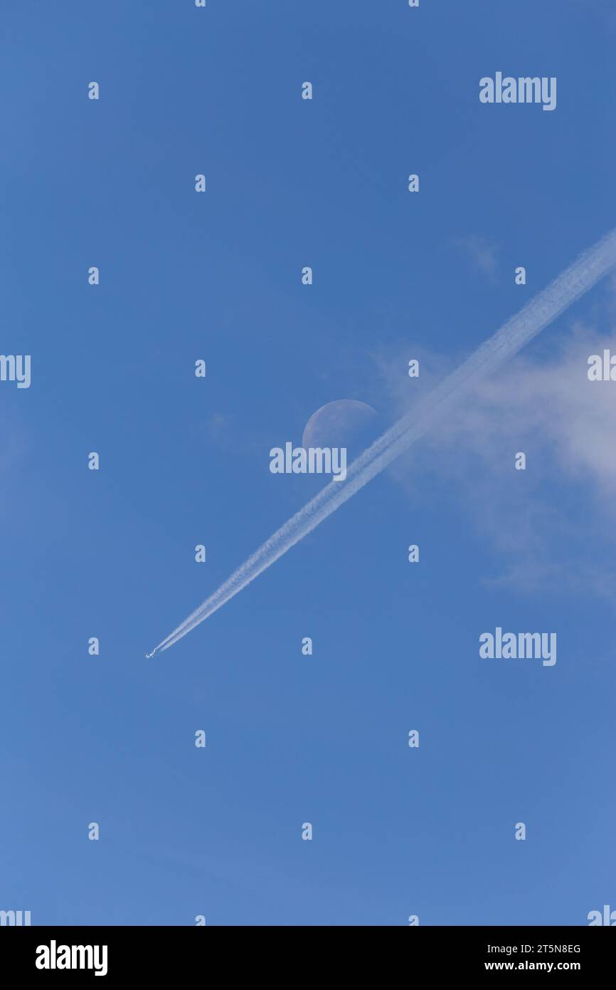 Una perfetta giornata estiva di sole con un aereo e sentieri di condensazione diretti verso una luna visibile in lontananza Foto Stock