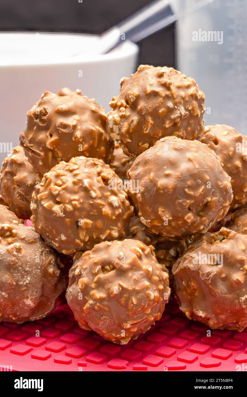 Un mucchio di grappoli di noci di cioccolato appoggiati su una placca da forno in silicone rosso Foto Stock