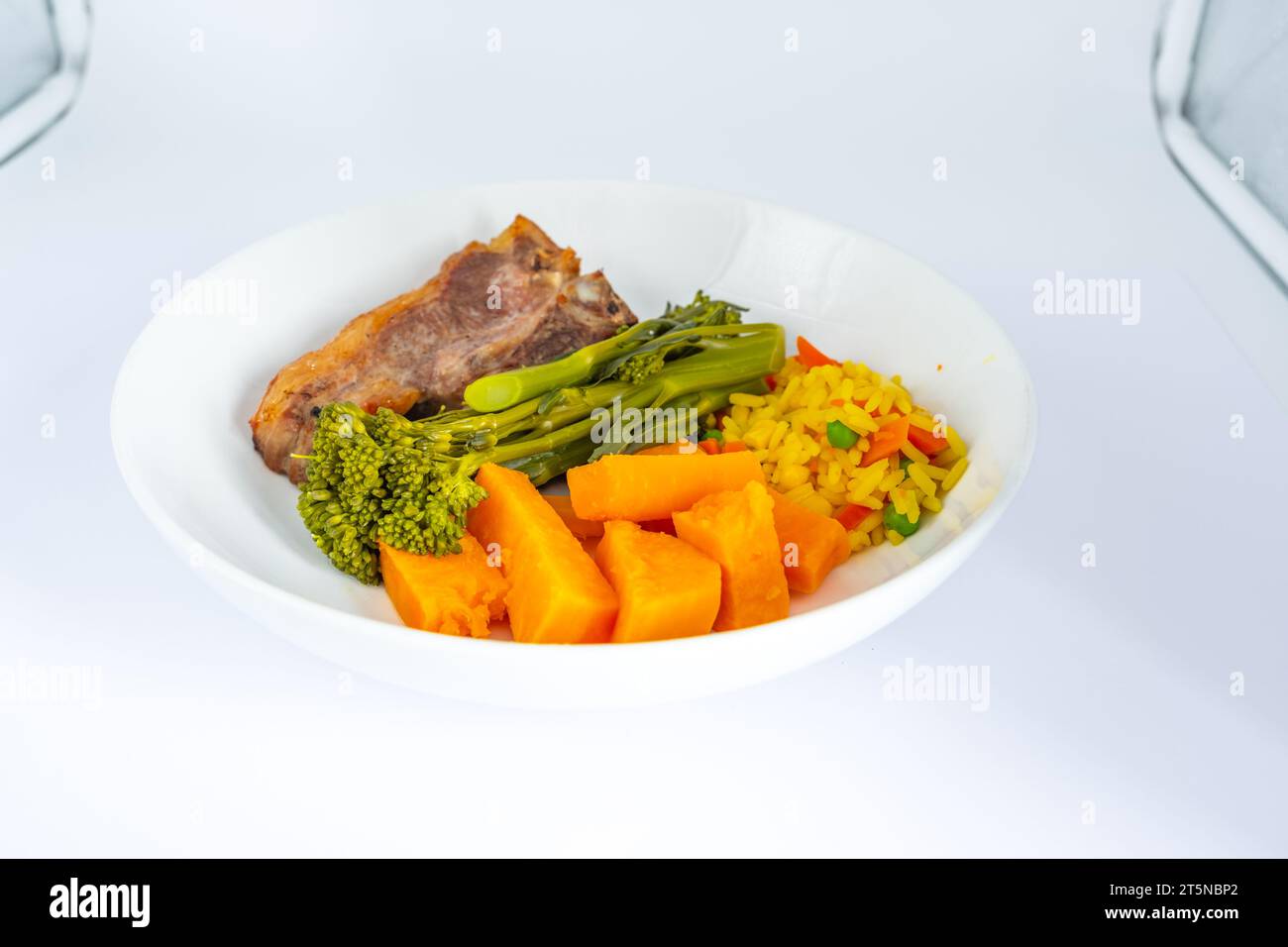 Costoletta di agnello arrosto con teneri broccoli di patate dolci carote e riso salato servito su un piatto bianco Foto Stock