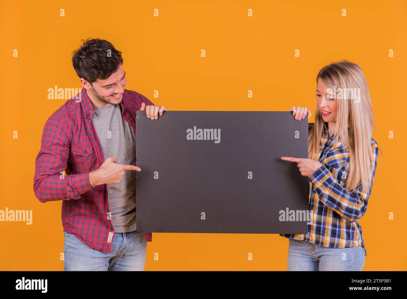 Primo piano di una giovane coppia che punta le dita con un cartello nero su sfondo arancione Foto Stock