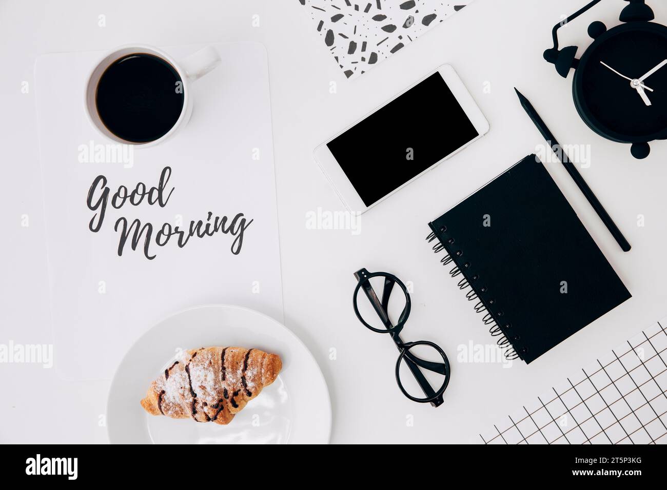 Tazza da caffè con croissant con carta del buon mattino, cancelleria da ufficio, scrivania bianca Foto Stock